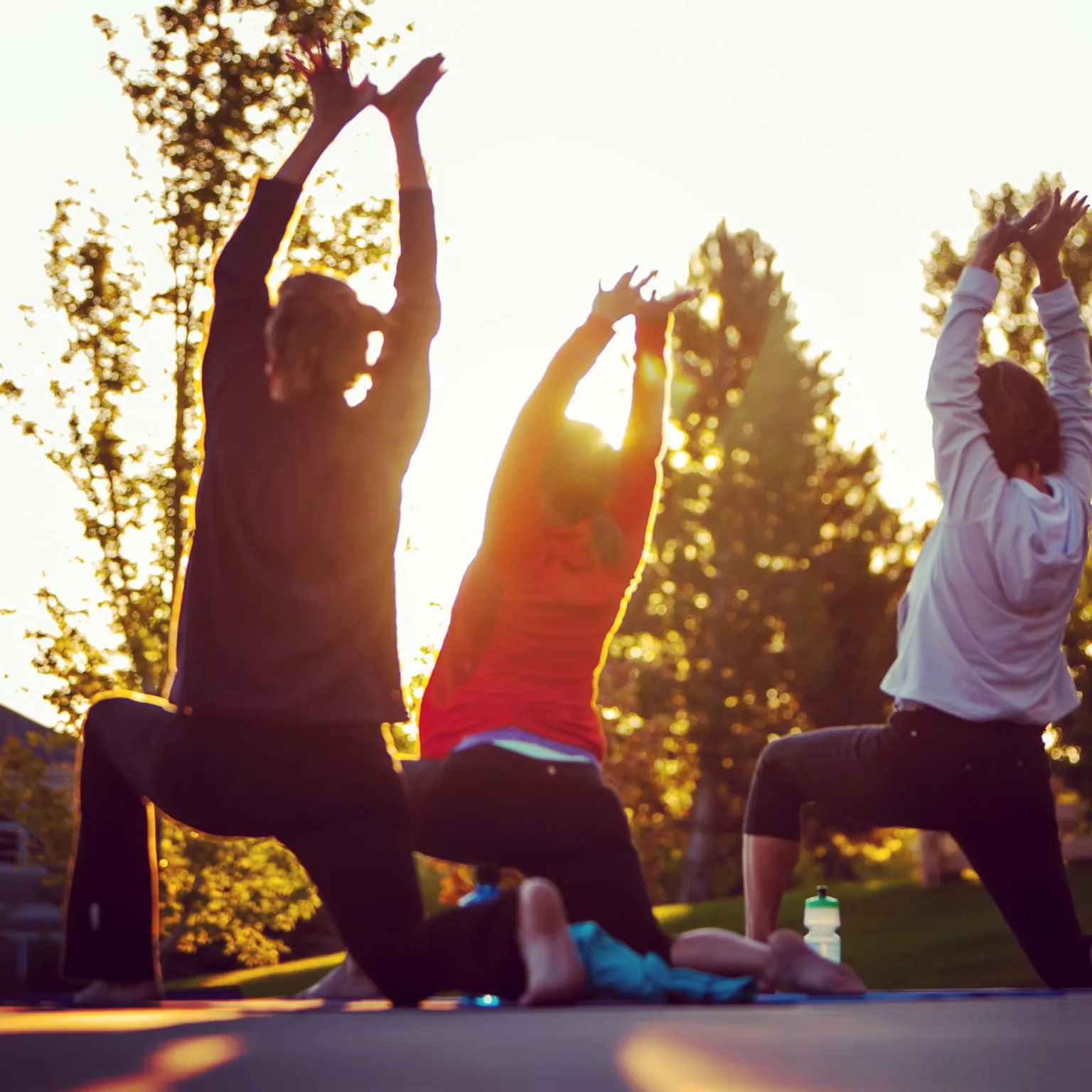 Three people in a low lunge with arms raised against a bright sky