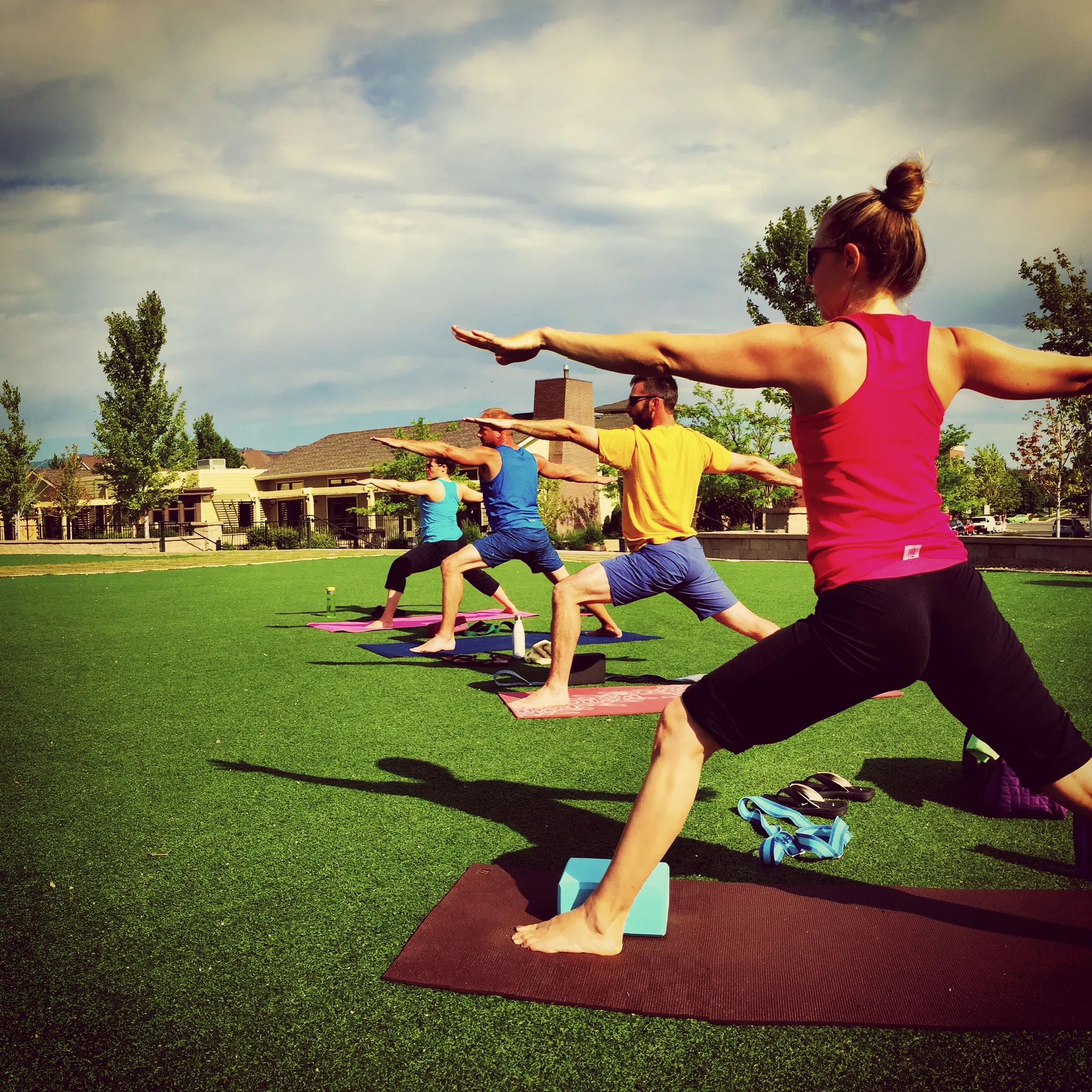 Outdoor yoga class in warrior two pose on a green lawn in a park