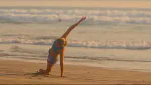 Woman in a side stretch on a beach at sunset with waves behind