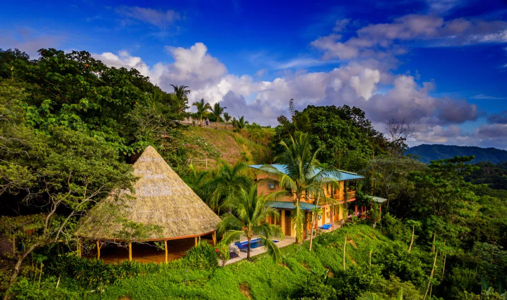 Aerial view of a thatched yoga pavilion and retreat house on a jungle hillside in Costa Rica