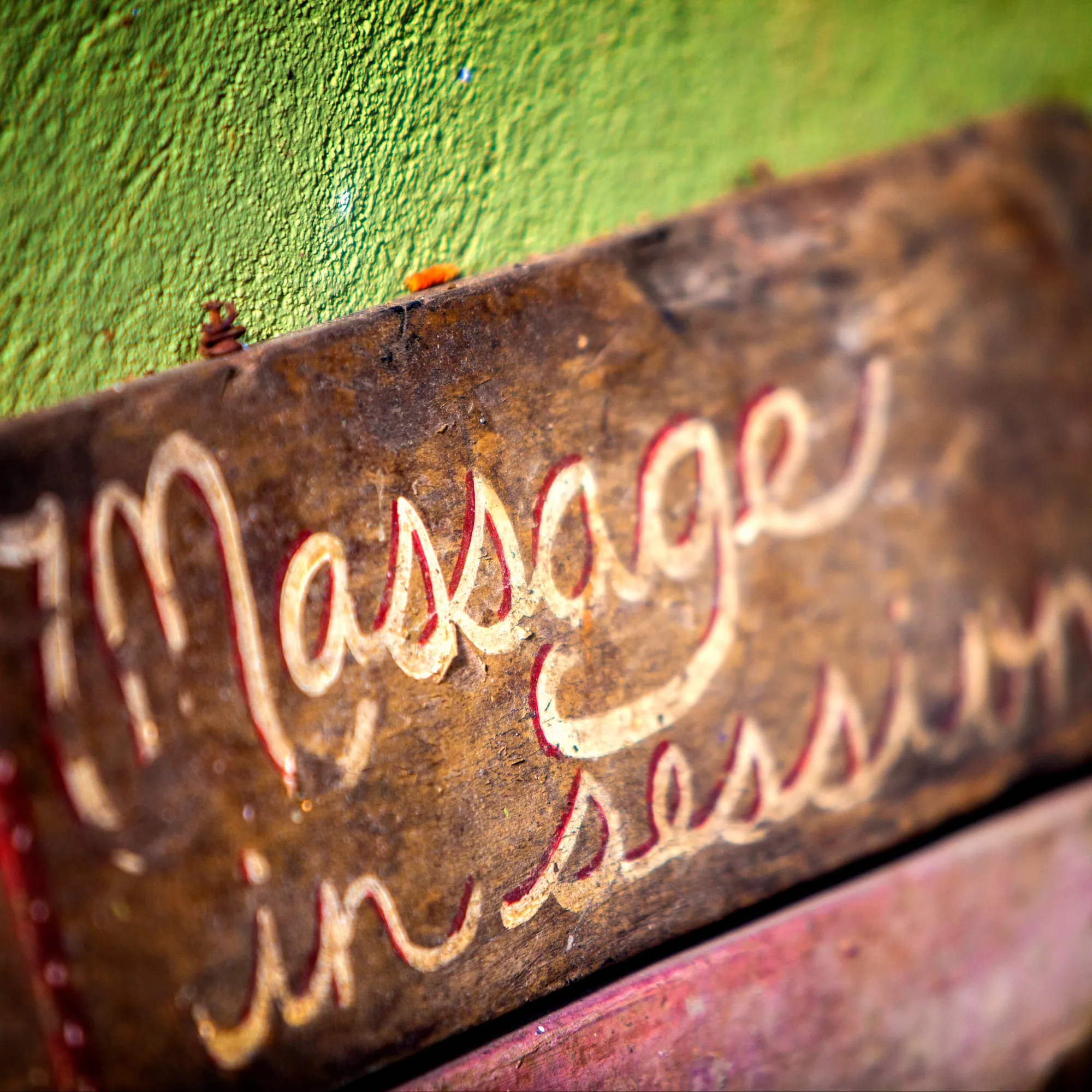 Hand-painted wooden sign reading Massage in session against a green wall