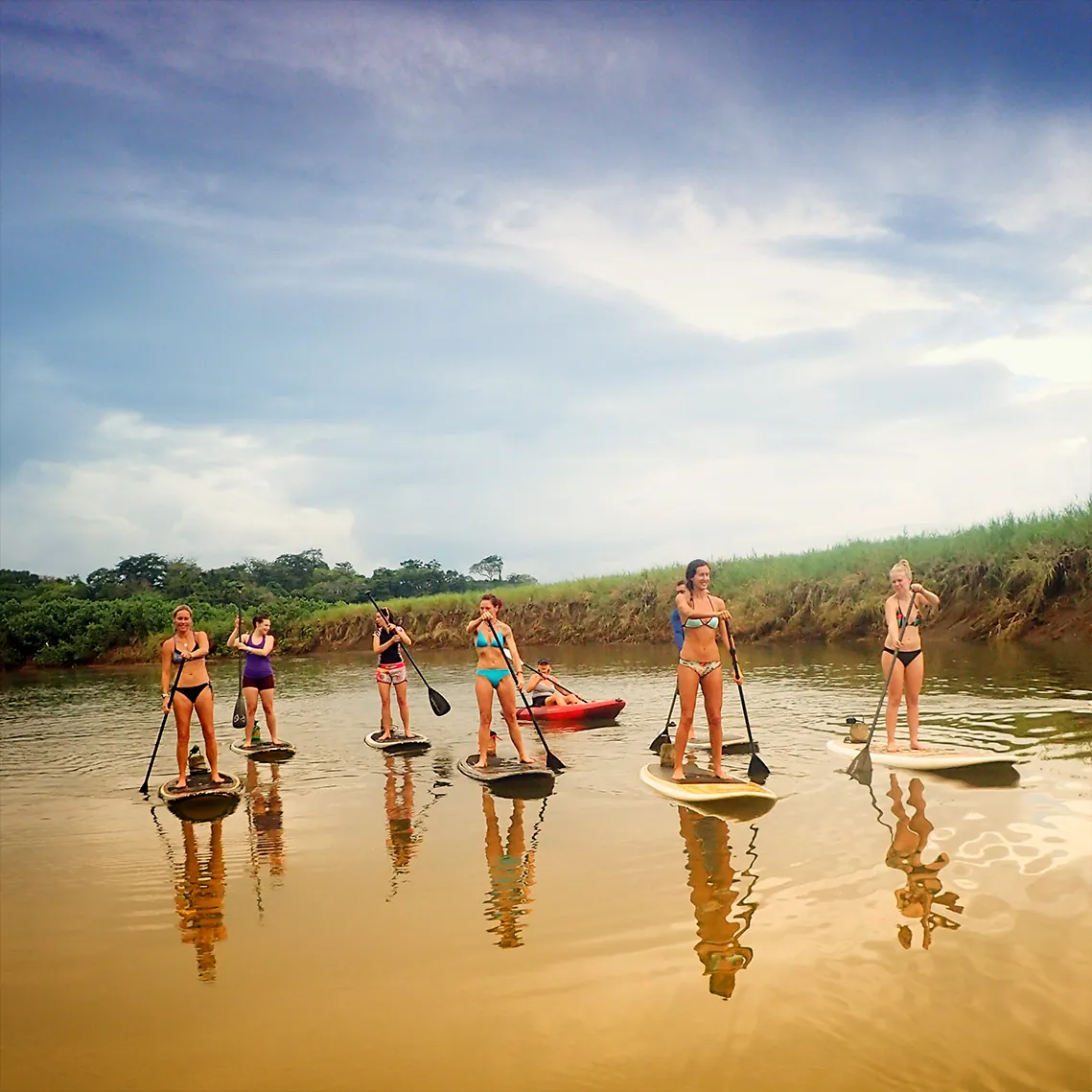 Retreat guests stand up paddleboarding on a calm river in Costa Rica
