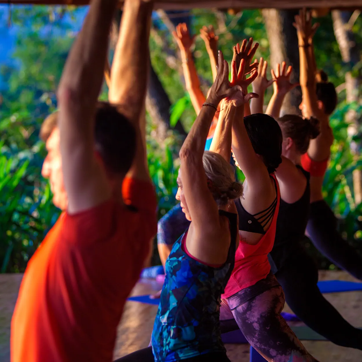 Retreat guests reaching arms overhead during an open-air yoga class with jungle behind them