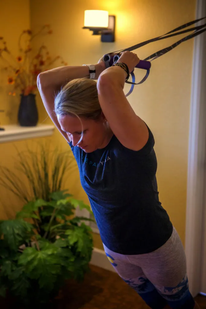 Woman pulling suspension straps overhead in a bent-over stretch indoors