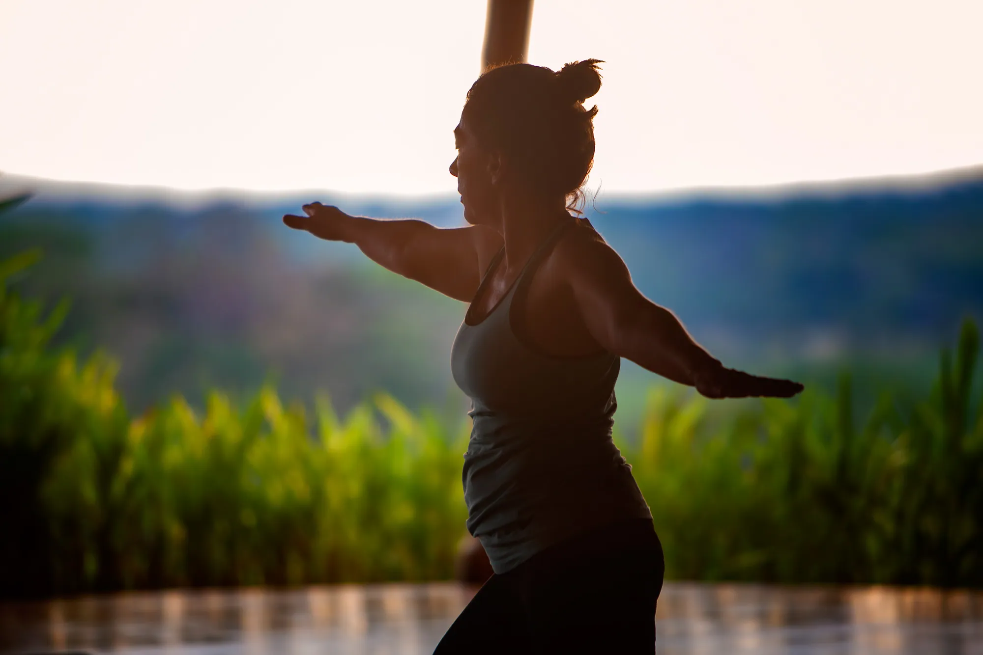 Silhouette of a retreat guest in a standing pose with arms outstretched against green hills