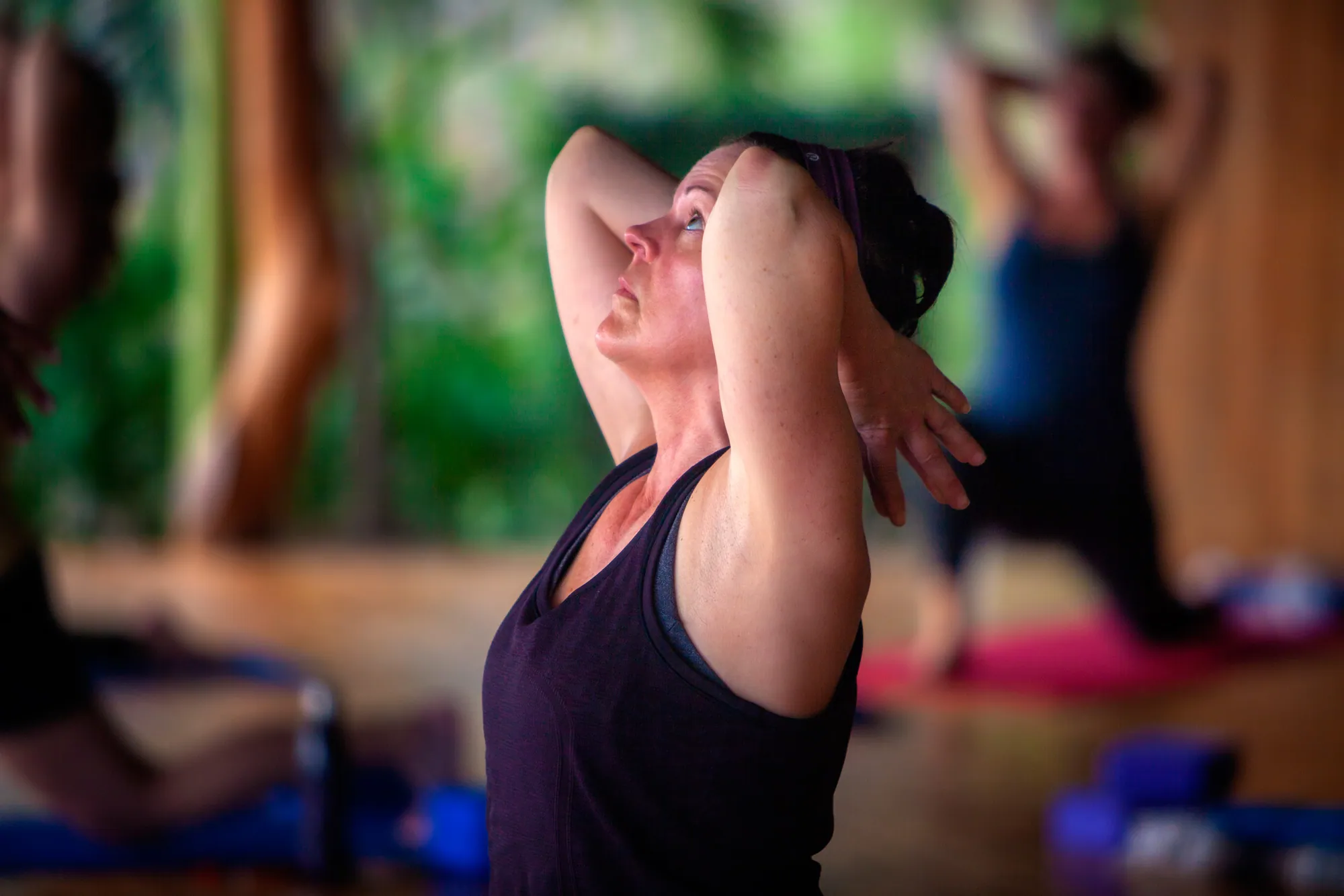 Retreat guest stretching with hands behind her head and eyes lifted during yoga class