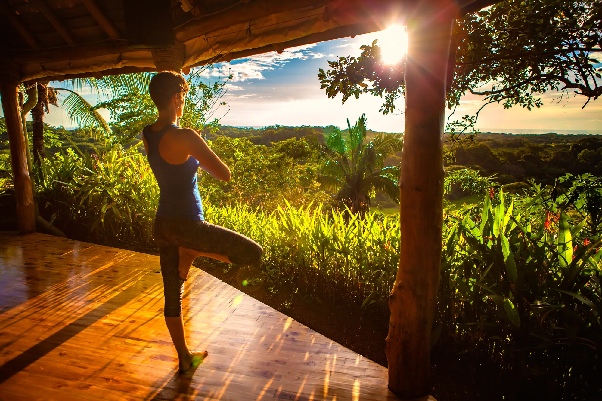 Retreat guest balancing on one leg in an open-air studio overlooking the jungle at sunset
