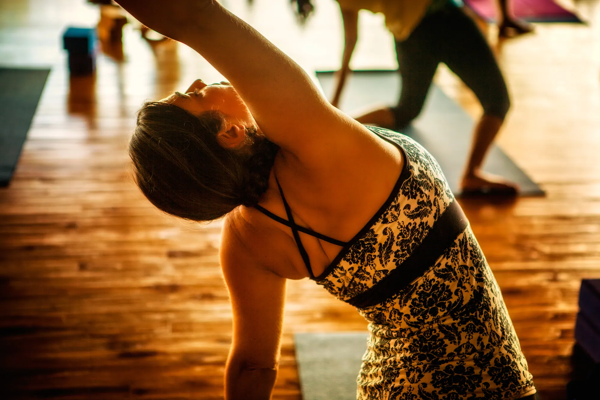Retreat guest in a reverse warrior side bend in a warm wood-floored studio