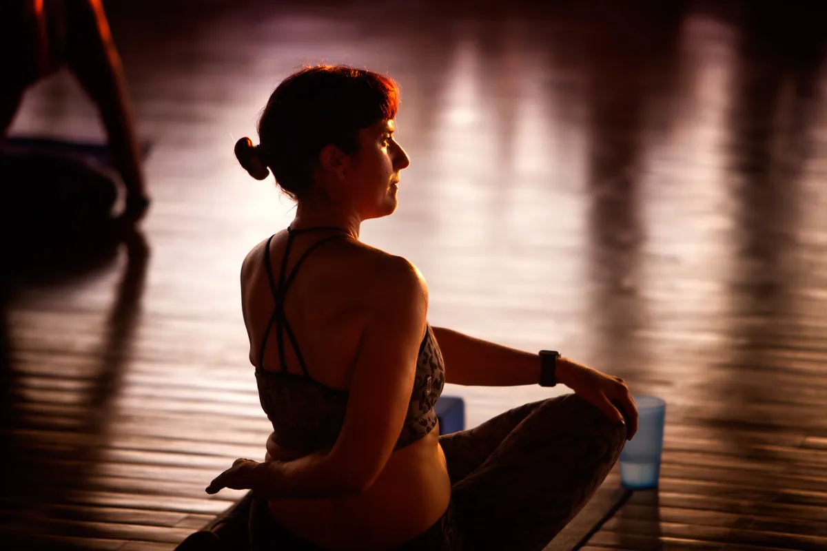 Retreat guest in a seated twist, softly backlit in a dark studio