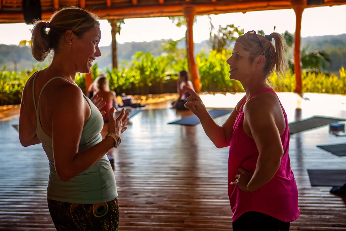 Two women chatting in an open-air yoga pavilion at sunset