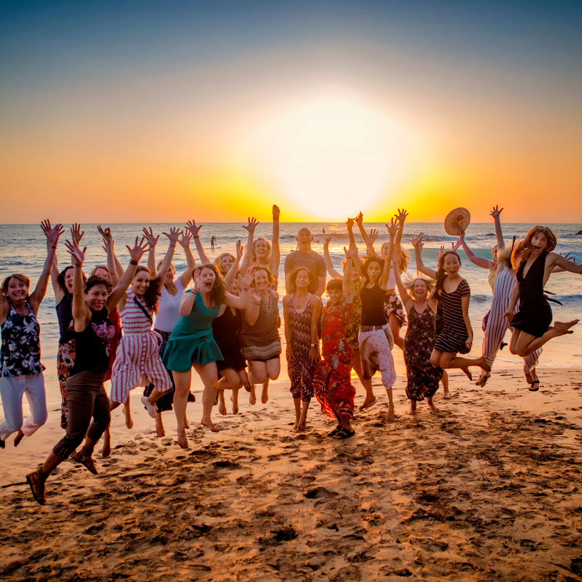 Large group jumping and cheering with arms up on a beach at sunset