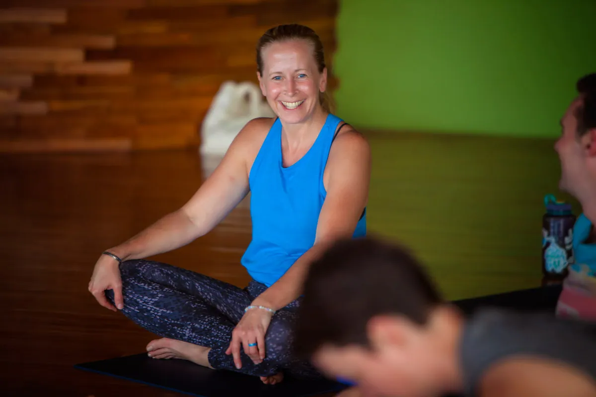 Smiling retreat guest in a blue tank top seated cross-legged on a mat