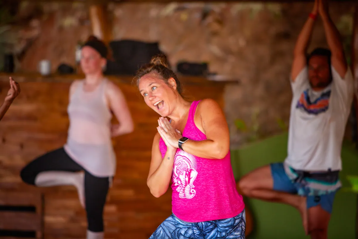 Retreat guest laughing in tree pose with hands at her heart beside other students