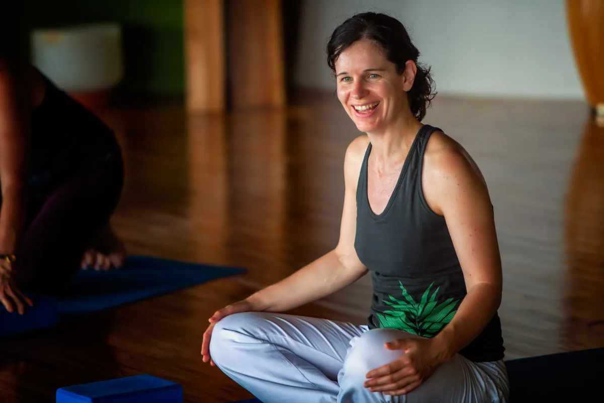 Smiling retreat guest seated cross-legged on a mat in a wood-floored studio