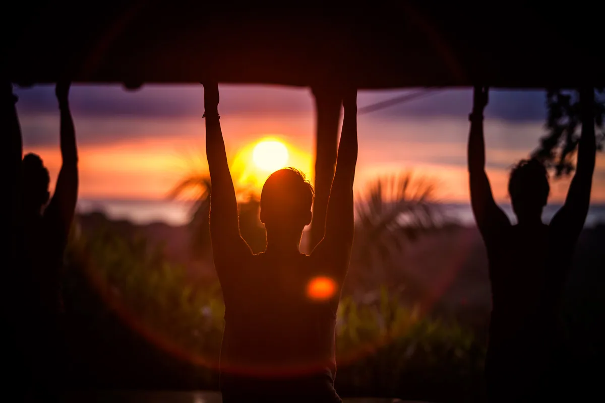 Silhouettes of retreat guests with arms raised against a tropical sunset