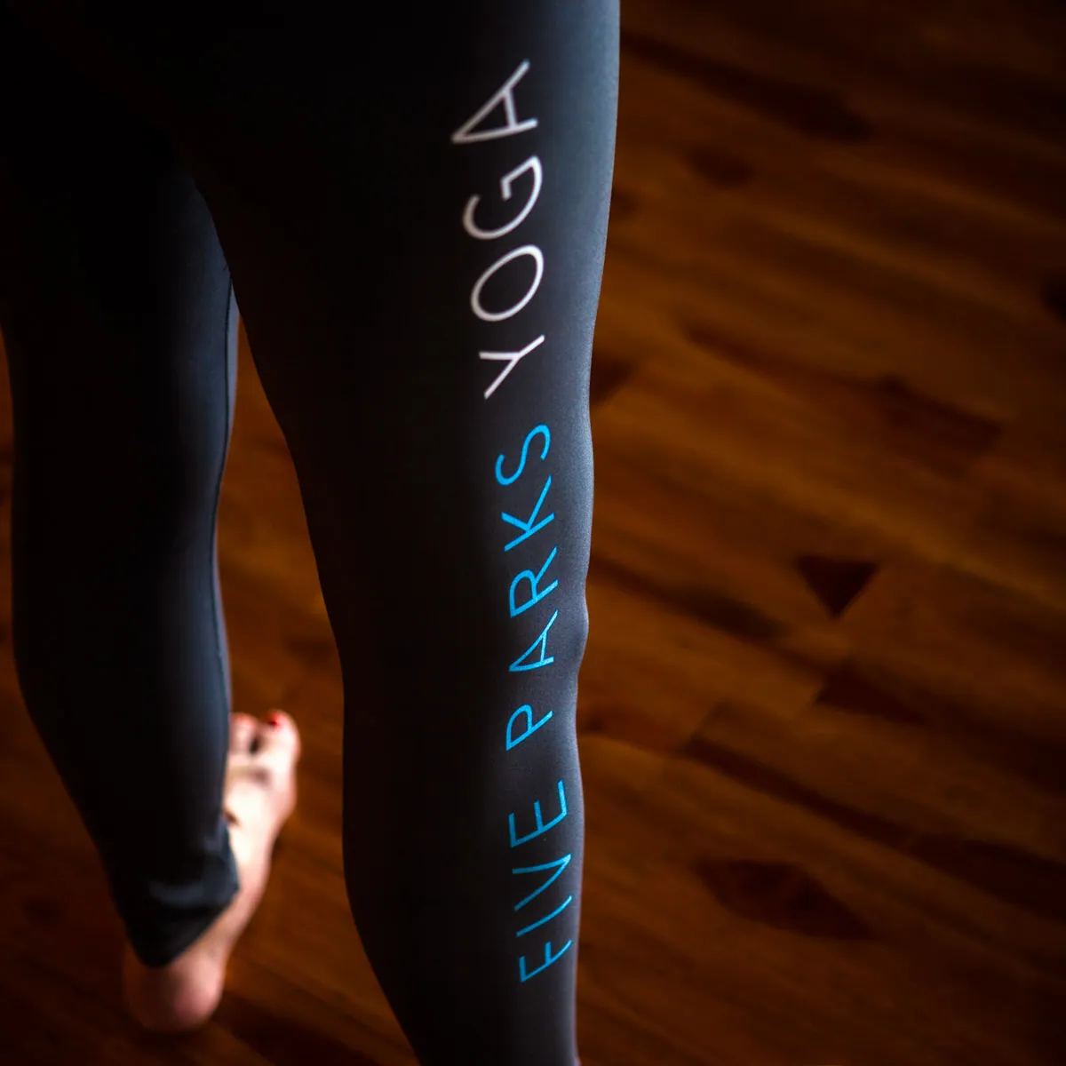Close-up of black Five Parks Yoga leggings on a wood floor