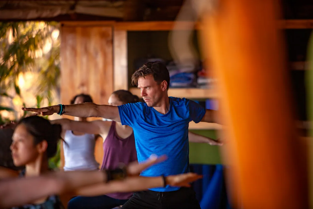 Retreat guest in warrior two with arms outstretched among other students
