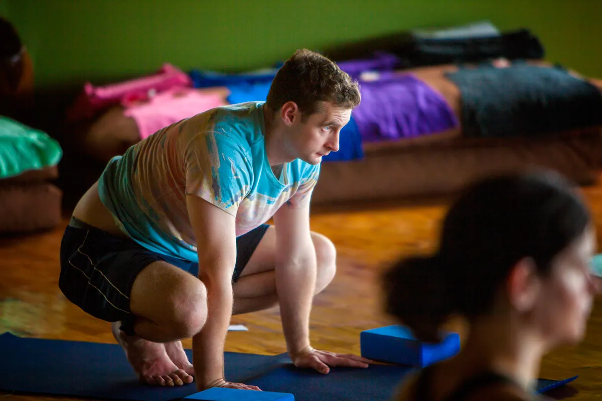 Retreat guest in a low squat on his mat with blocks and blankets behind him