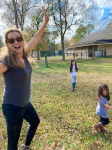 Smiling woman stretching in a park with two children running behind her