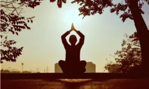 Silhouette of a person in prayer pose at sunset beneath trees