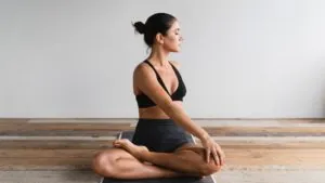 Woman seated in a cross-legged yoga pose with eyes closed in a bright room