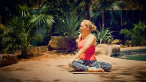 Woman sitting cross-legged beside the pool at Casa Colorado, surrounded by palms