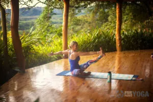 Woman in a seated yoga pose on a wooden deck above a jungle valley