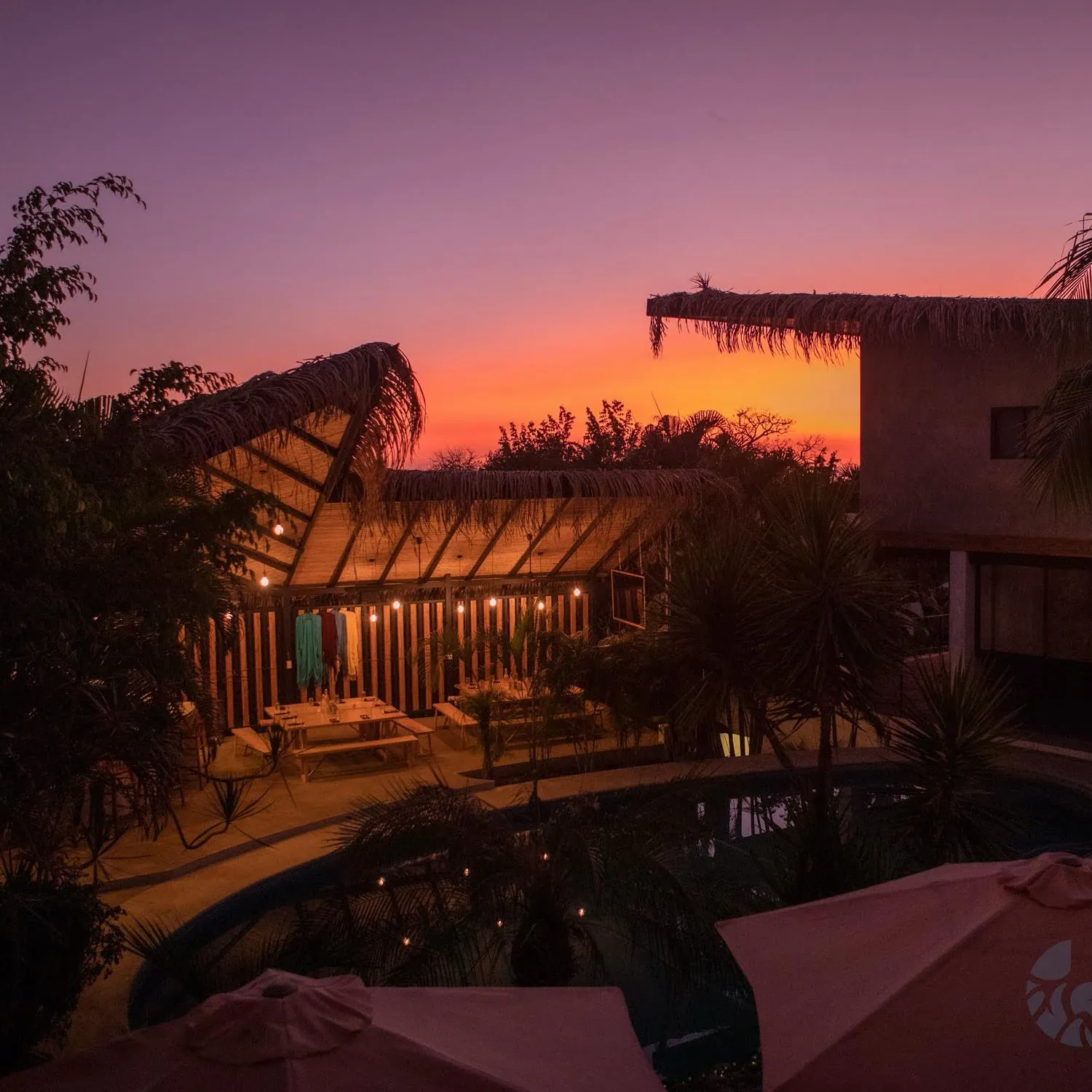 Thatched-roof buildings and pool glowing at sunset
