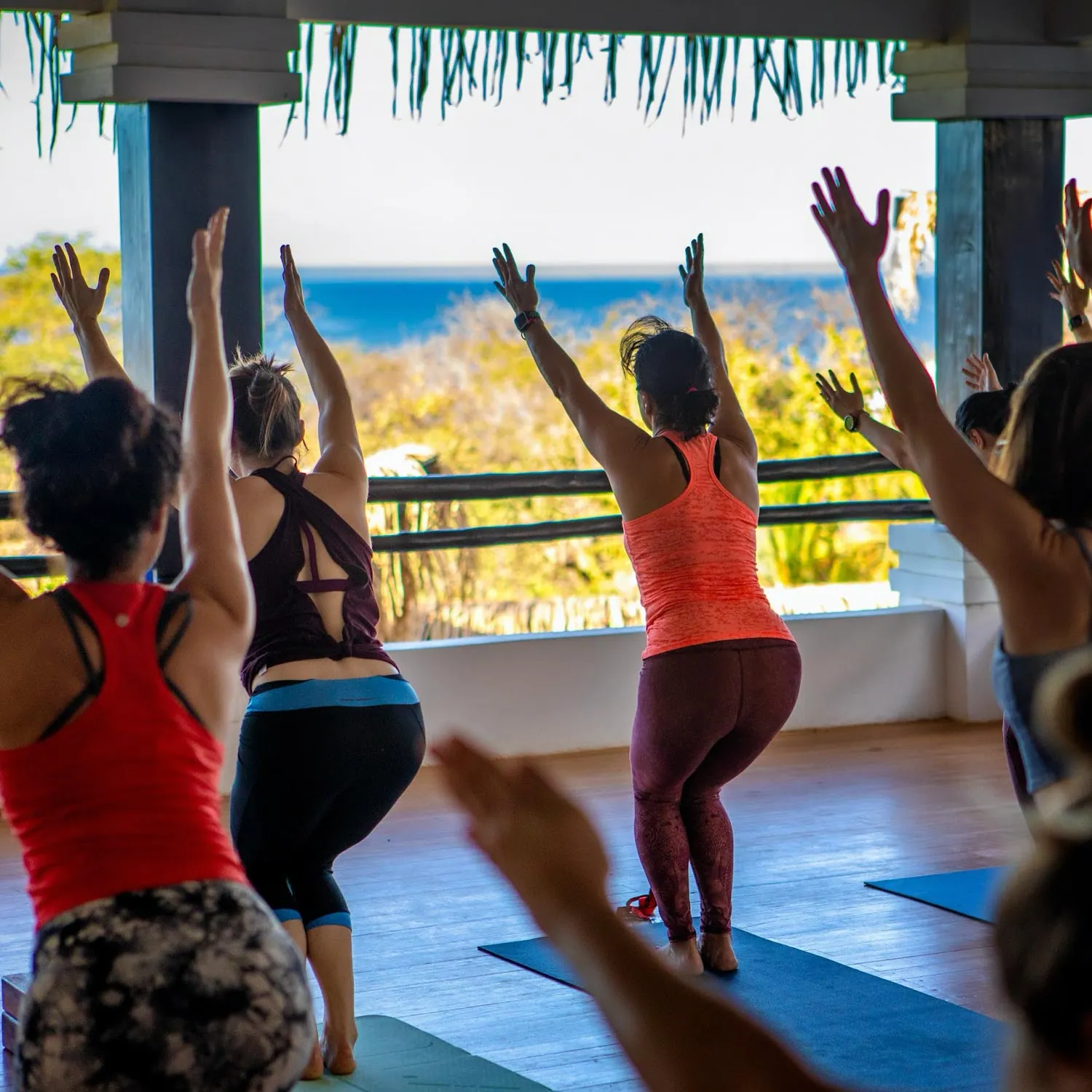Guests raising their arms in chair pose on mats with an ocean view