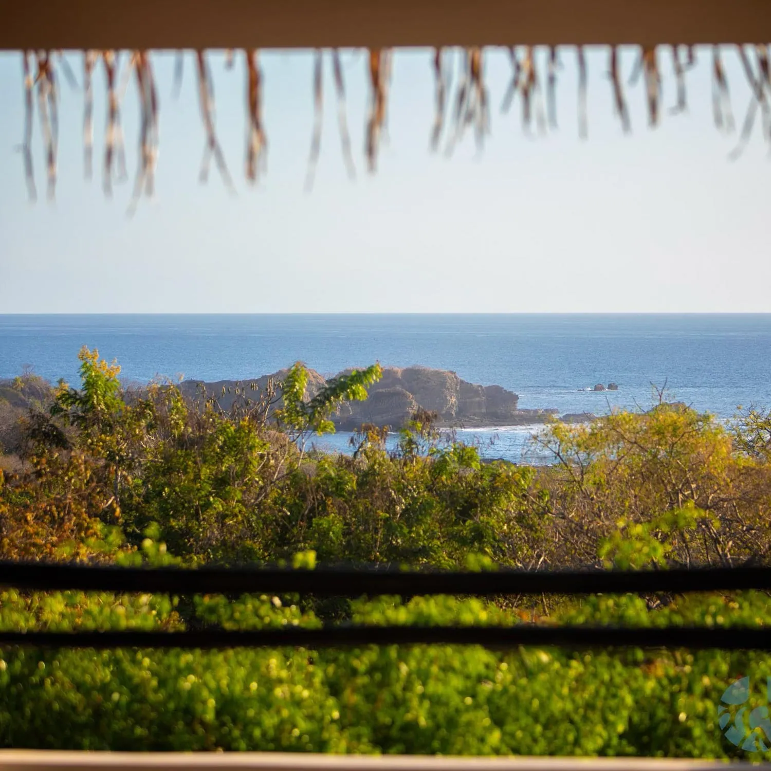 Ocean view through a thatched roof edge and railing