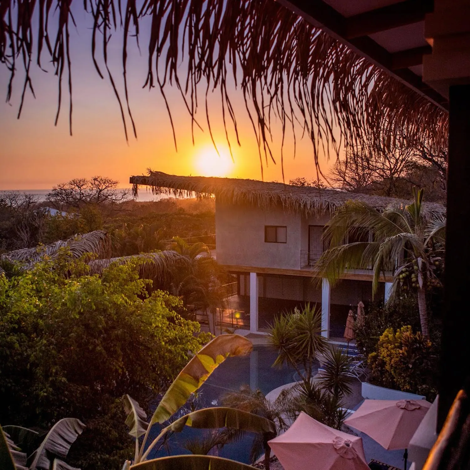 Sun setting behind a resort building and pool