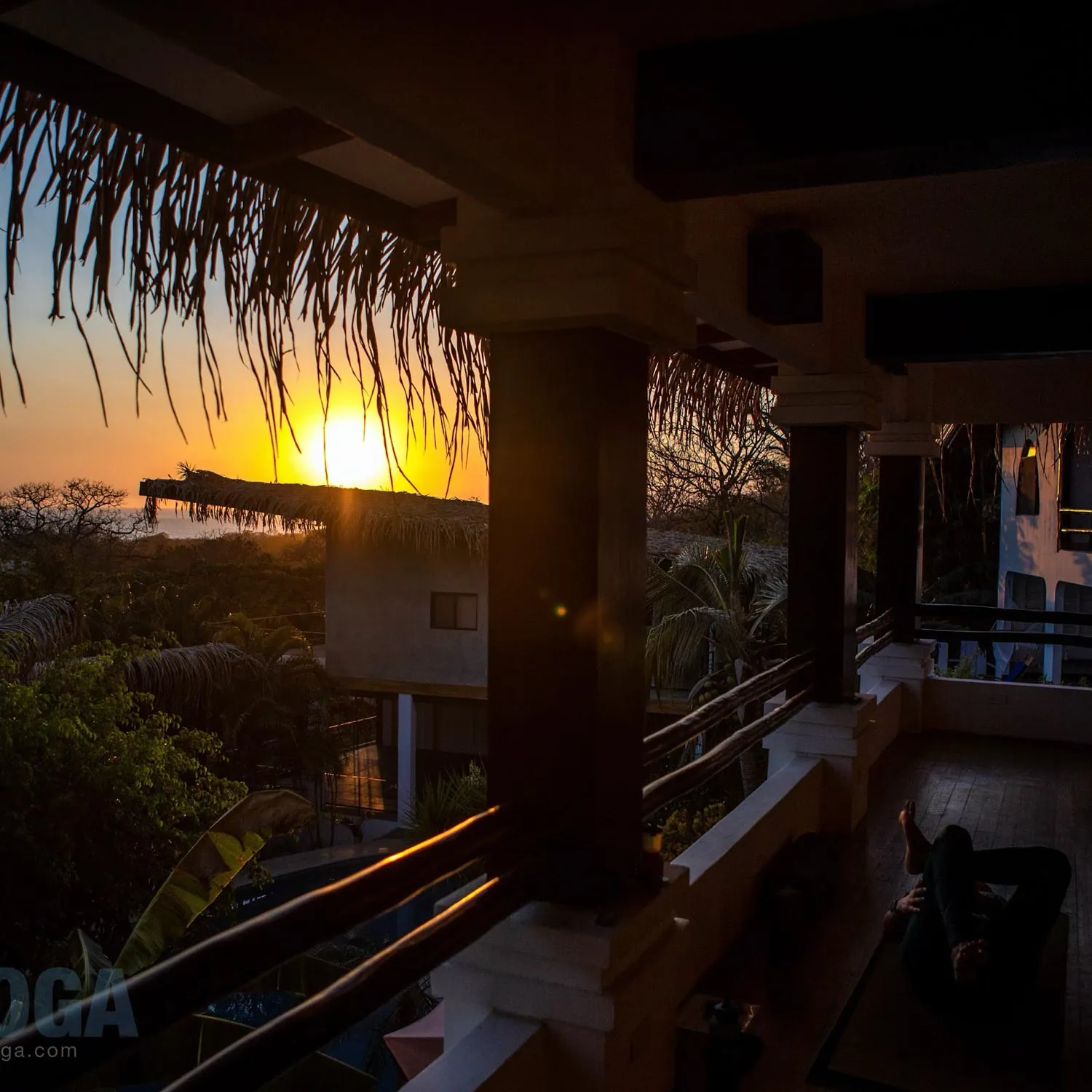Sun setting beyond a thatched roof and railing
