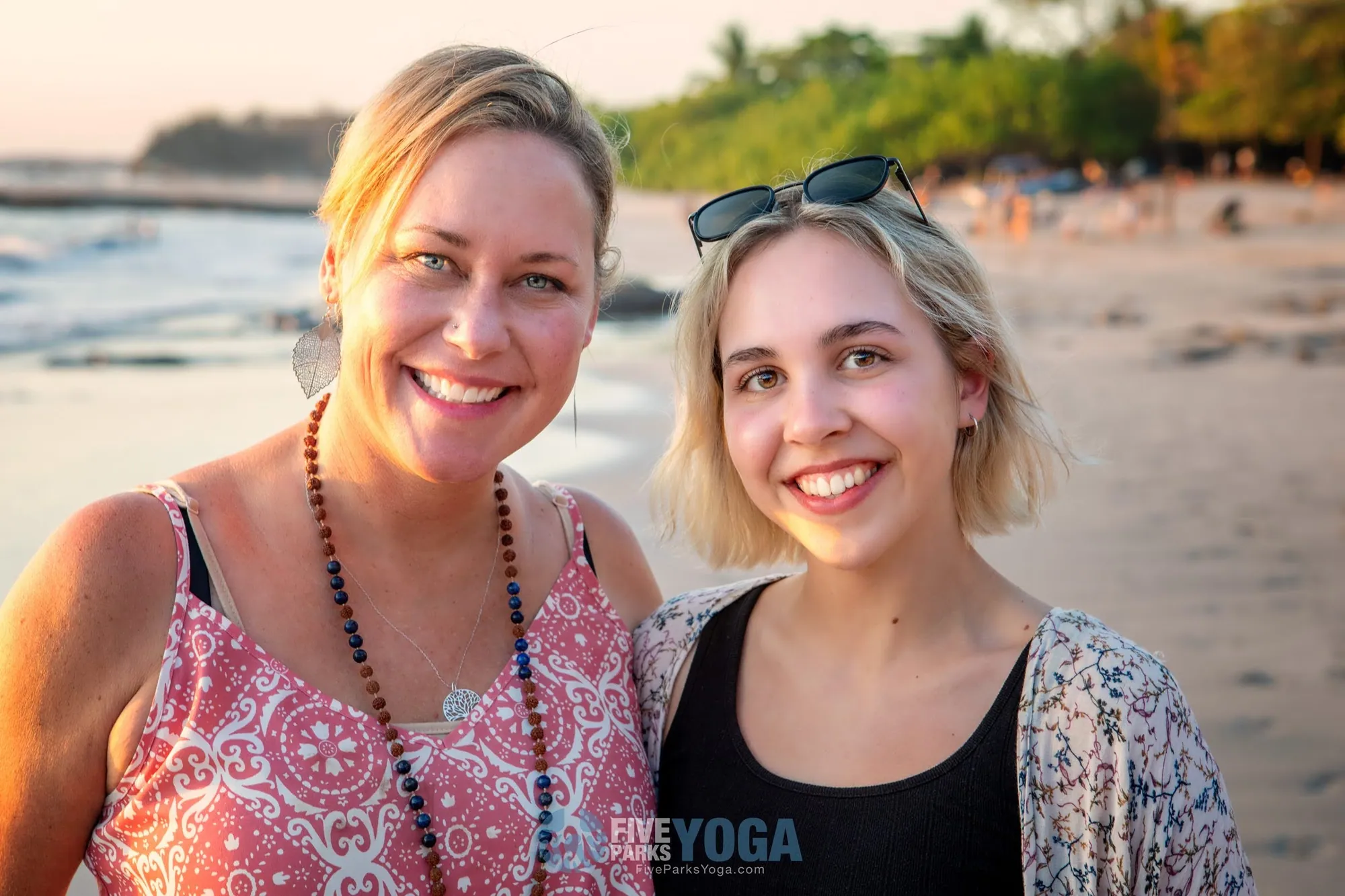 Two smiling women posing together on a beach