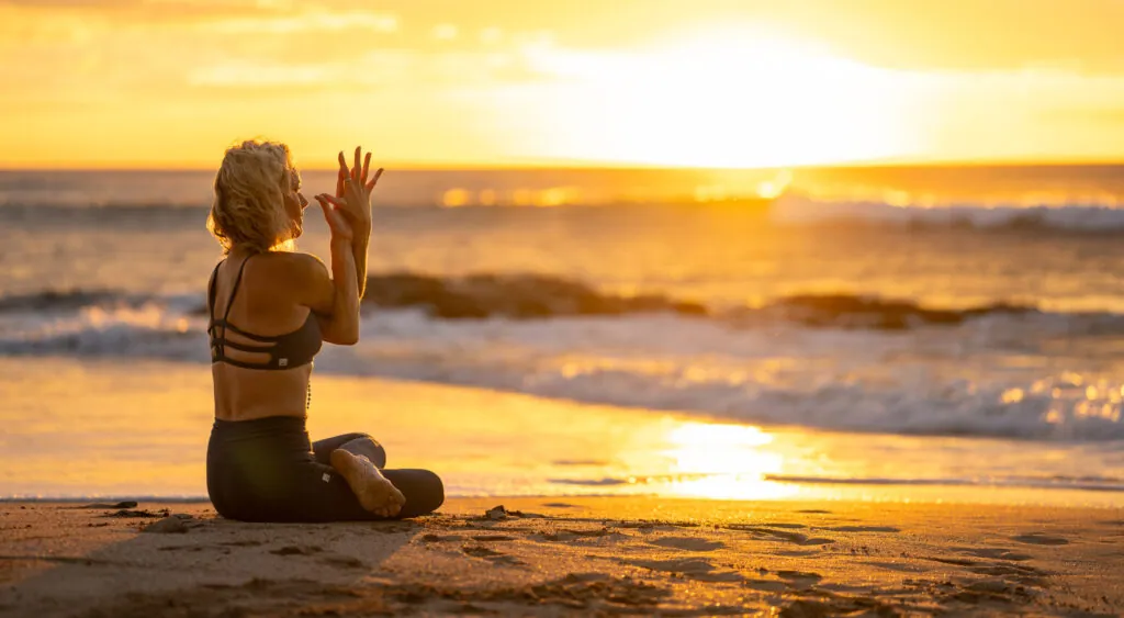 Woman sitting in prayer pose on a beach at sunset