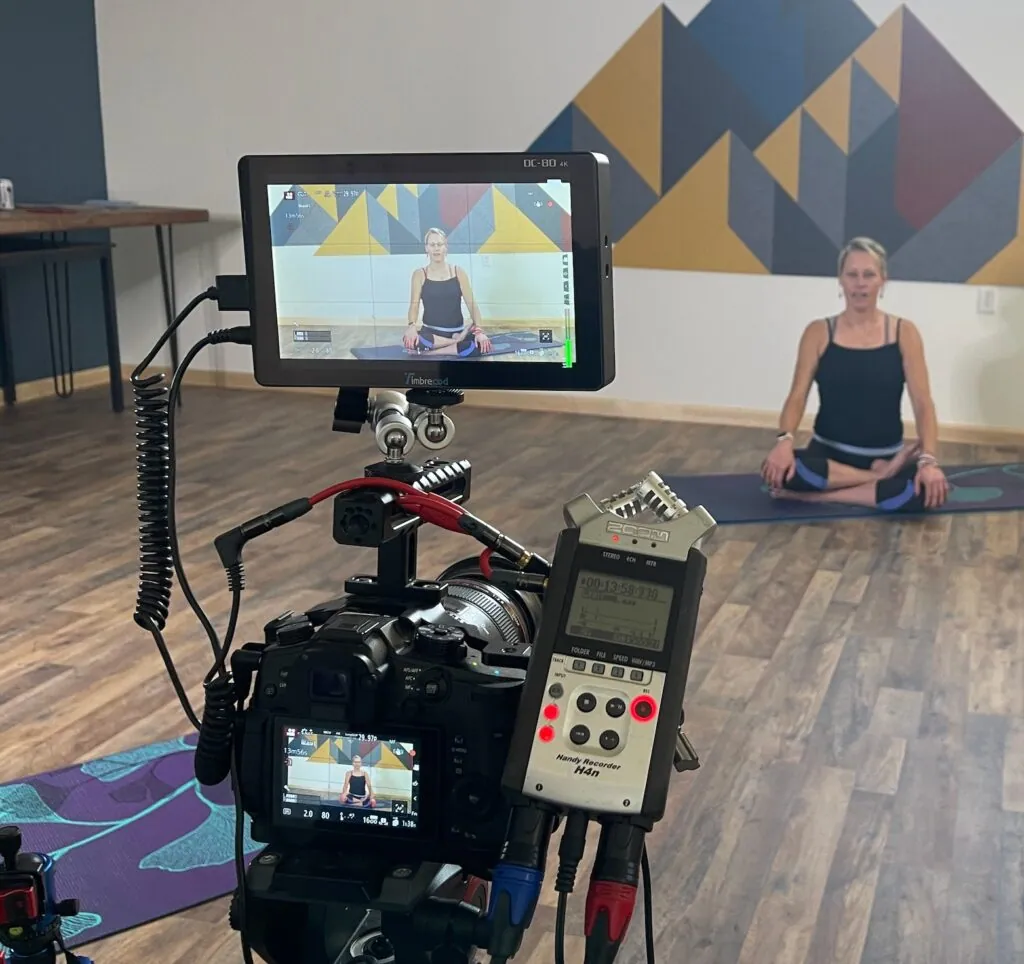 Erin Sampson teaching on a mat in a studio with a camera and monitor in the foreground