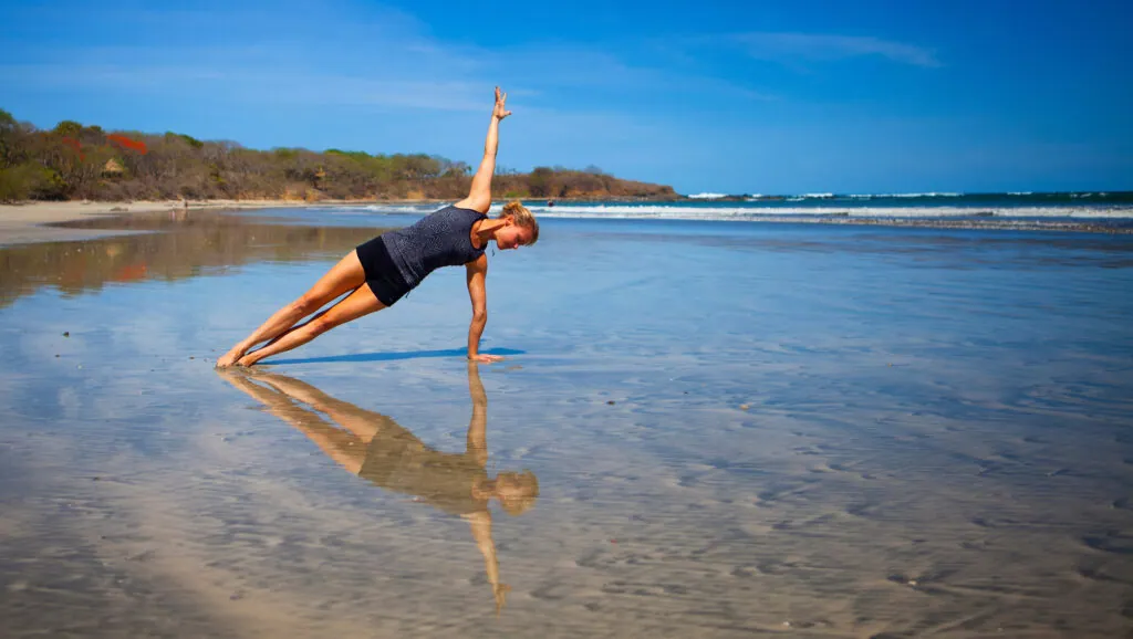Woman in side plank on wet sand at the beach, reflected in the water