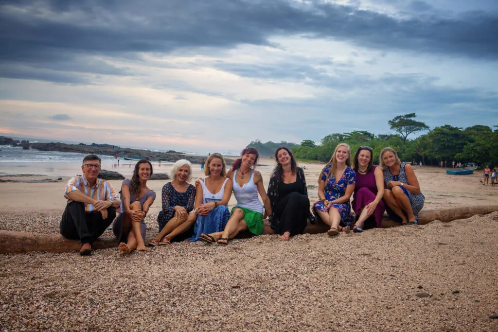 Group of yoga teacher training students sitting together on a log at the beach