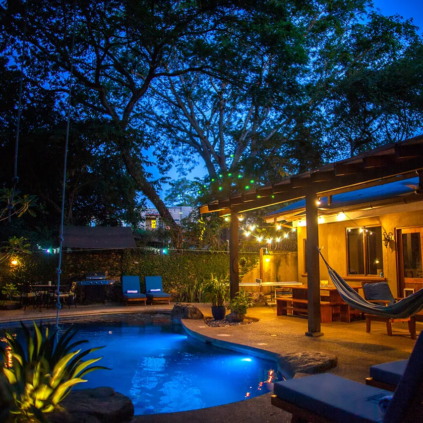 Lit pool and covered patio with hammock at dusk