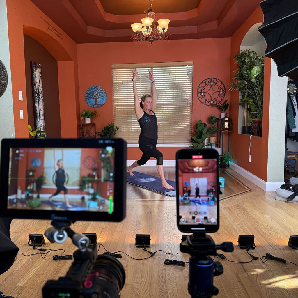 Erin Sampson teaching in a warrior pose in the studio, camera monitor in foreground
