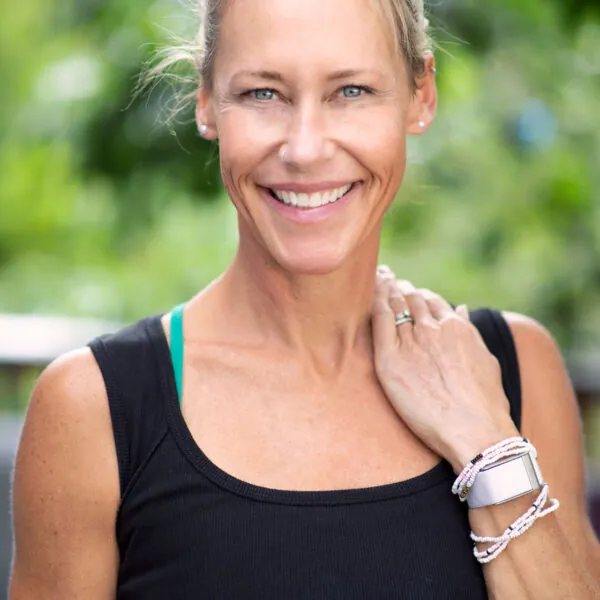 Erin Sampson smiling outdoors in a black tank top with greenery behind her