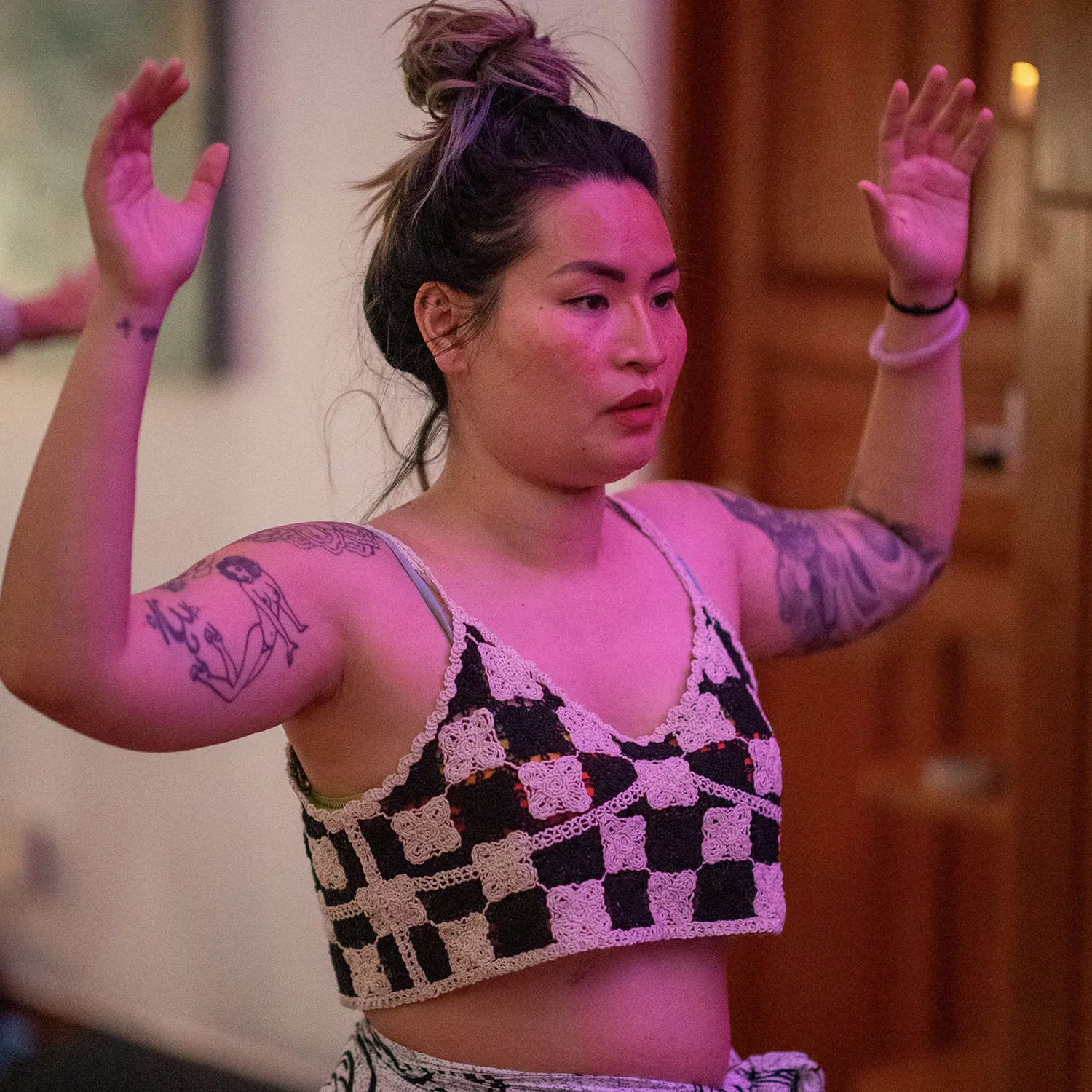 Woman with tattoos raising both hands in a studio lit with pink light