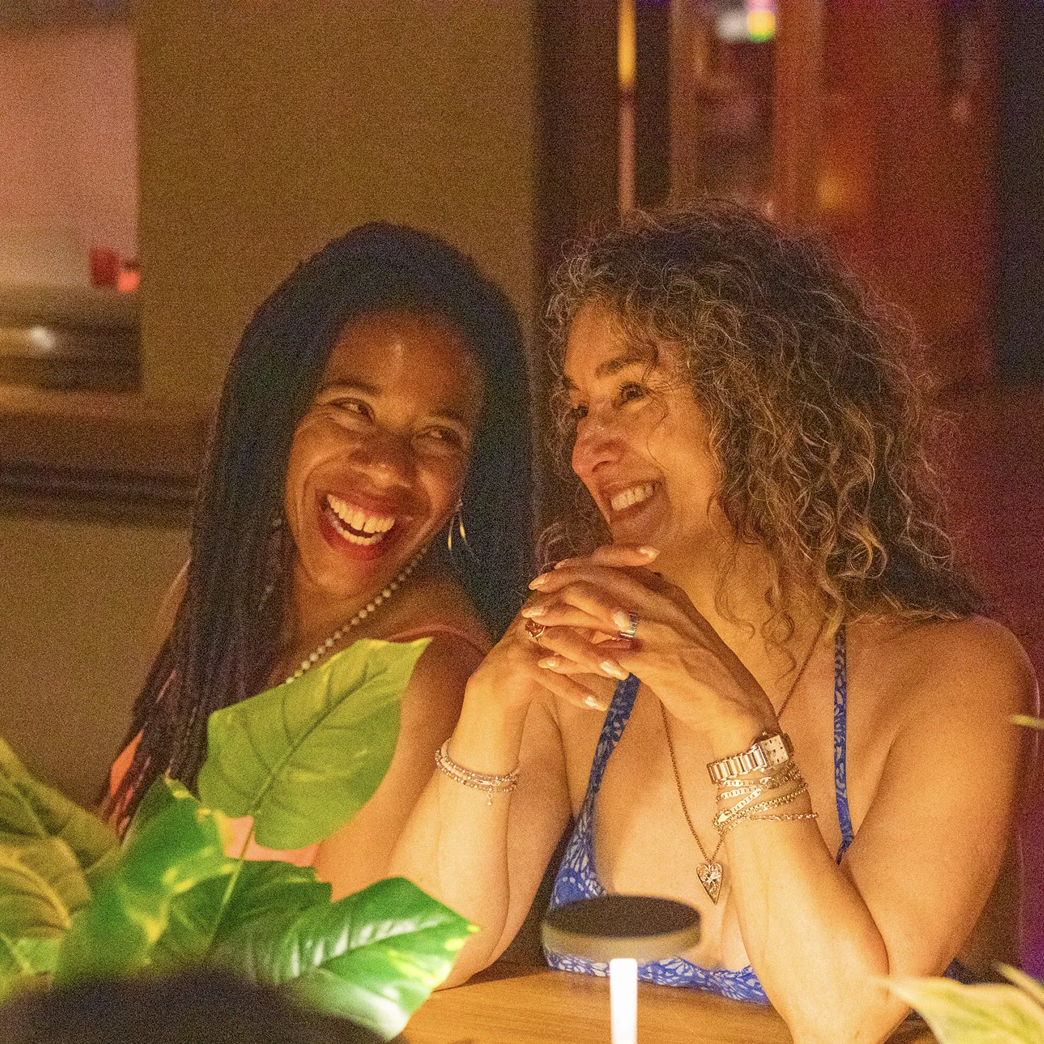 Two women laughing together at a table in warm evening light