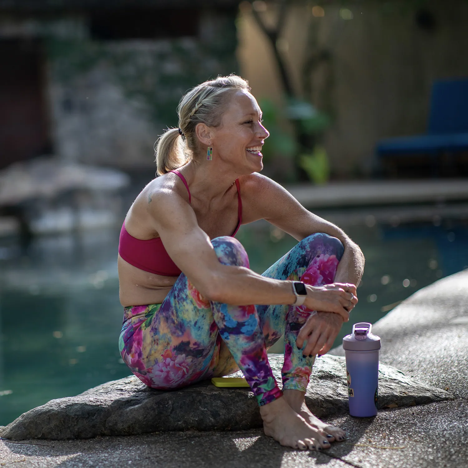 Erin Sampson laughing, sitting on a rock beside a pool in colorful leggings