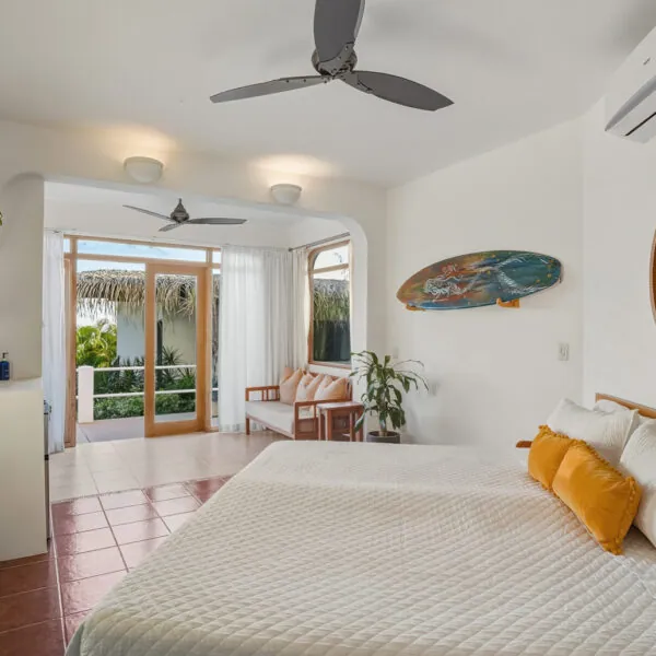 Bright guest room with a large bed, ceiling fans and a surfboard on the wall at Casas Kismet, Nosara